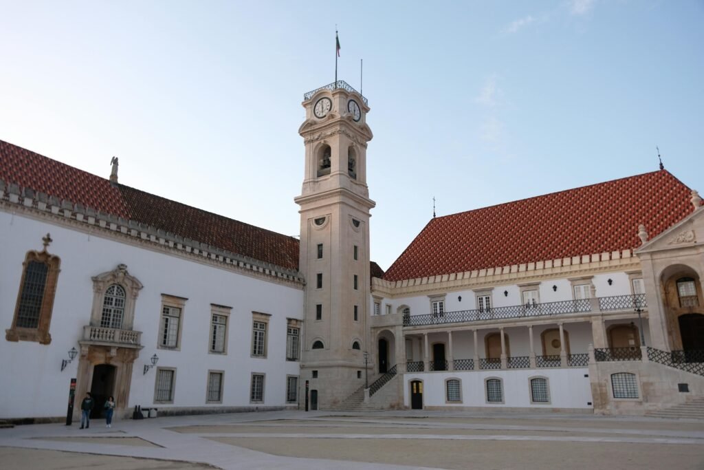 The iconic clock tower at the University of Coimbra, Portugal under a clear blue sky.