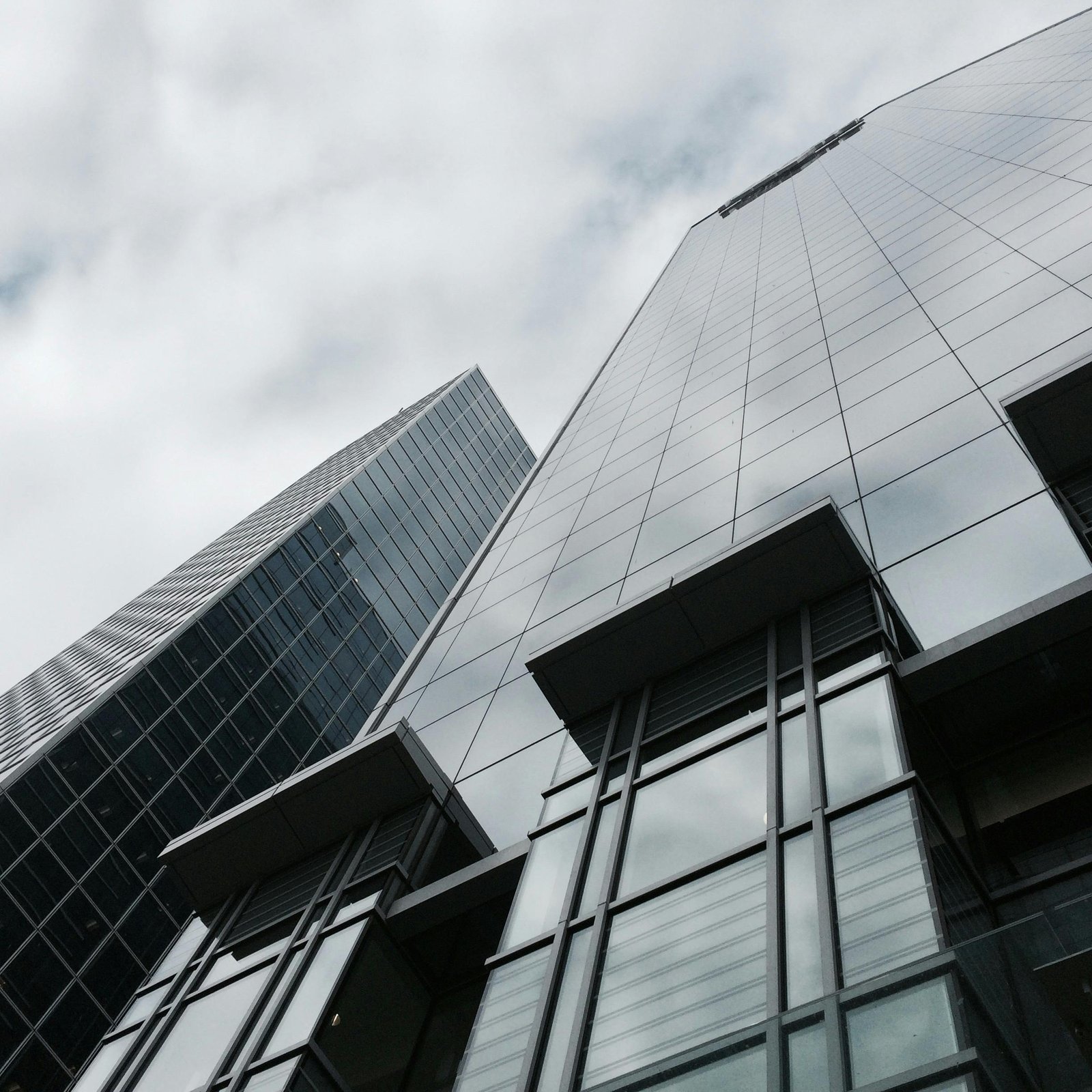 Low angle view of two modern skyscrapers with glass facades against a cloudy sky.