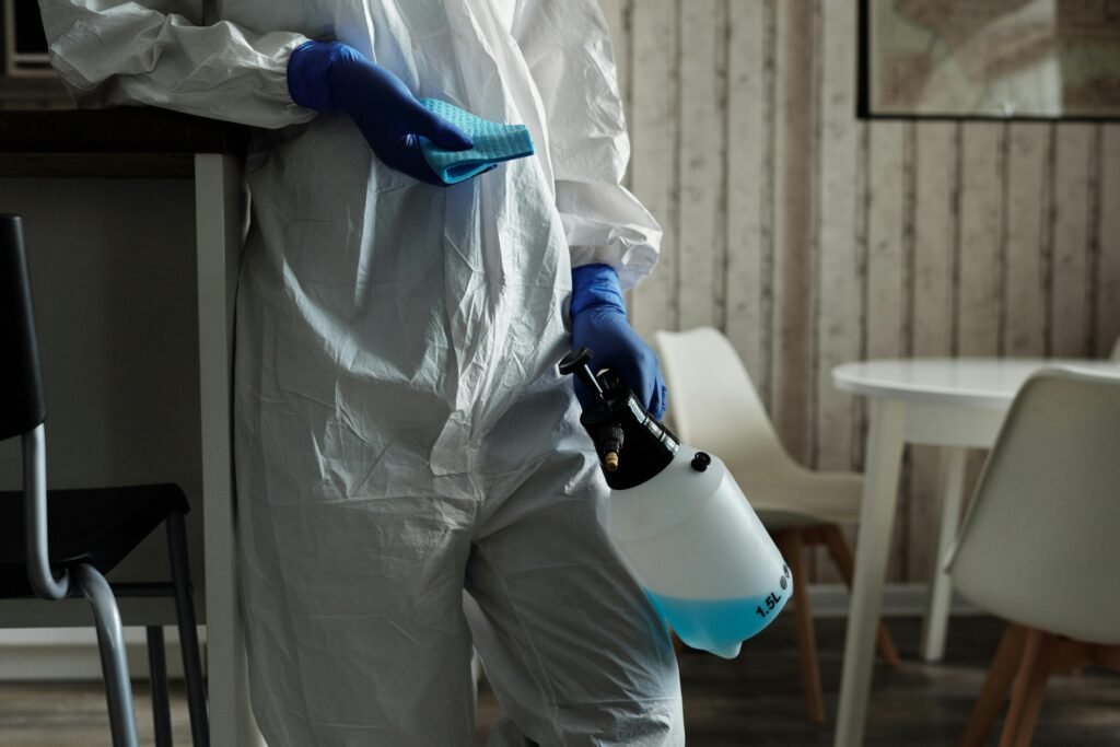 Person in protective gear disinfecting with spray in home setting.